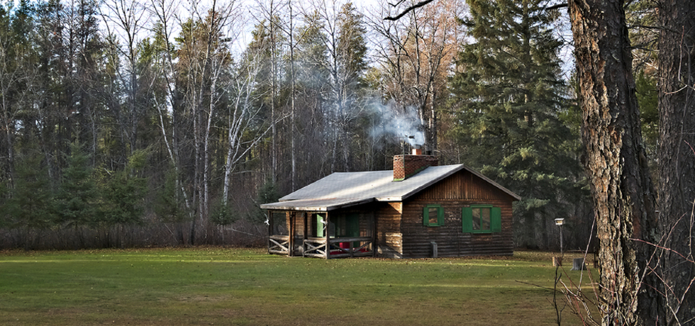 A cabin with smoke coming from its chimney in a wooded area.