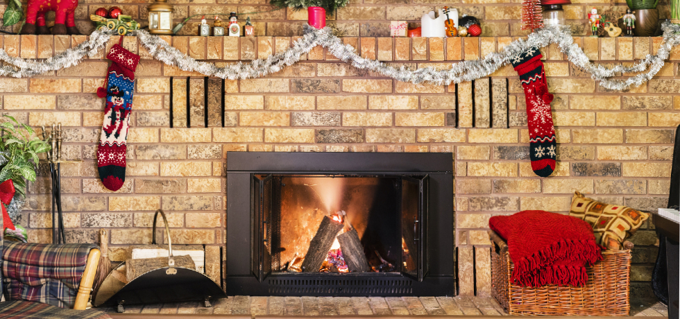A fireplace and brick mantle with stockings and garland hung on them.