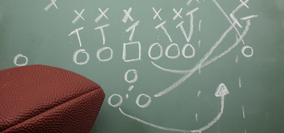 The Xs and Os of a football play on a chalkboard with a football nearby.