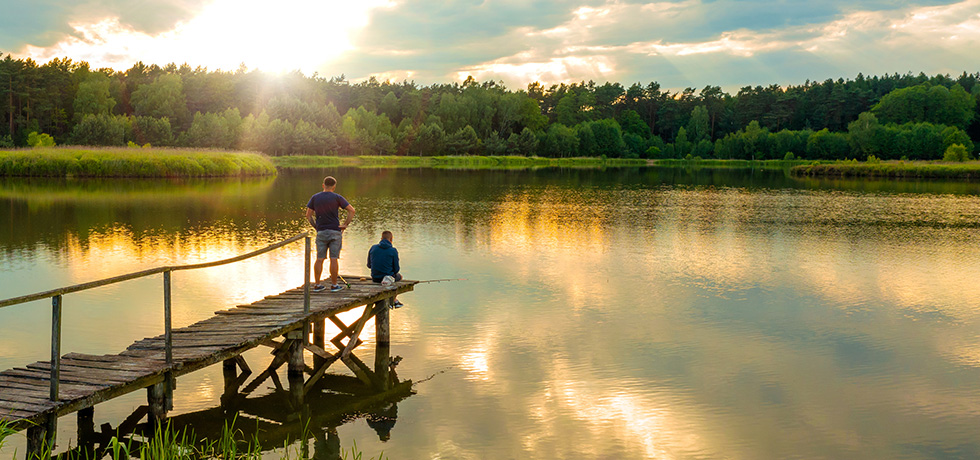 A pair of men fish off a pier on a serene lake.