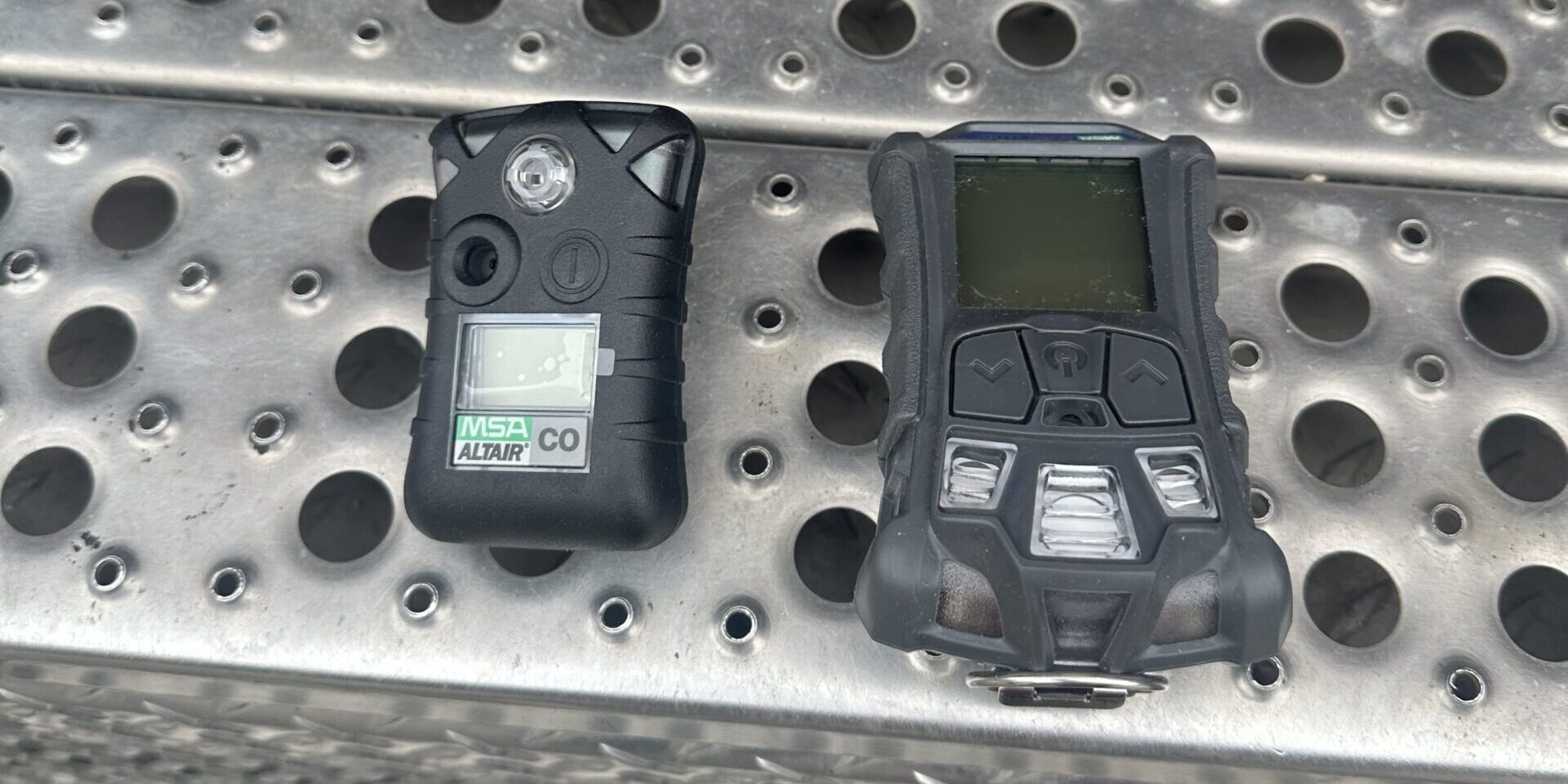 A black multi-gas detector and calibration unit laying on top of a steel-grated step.