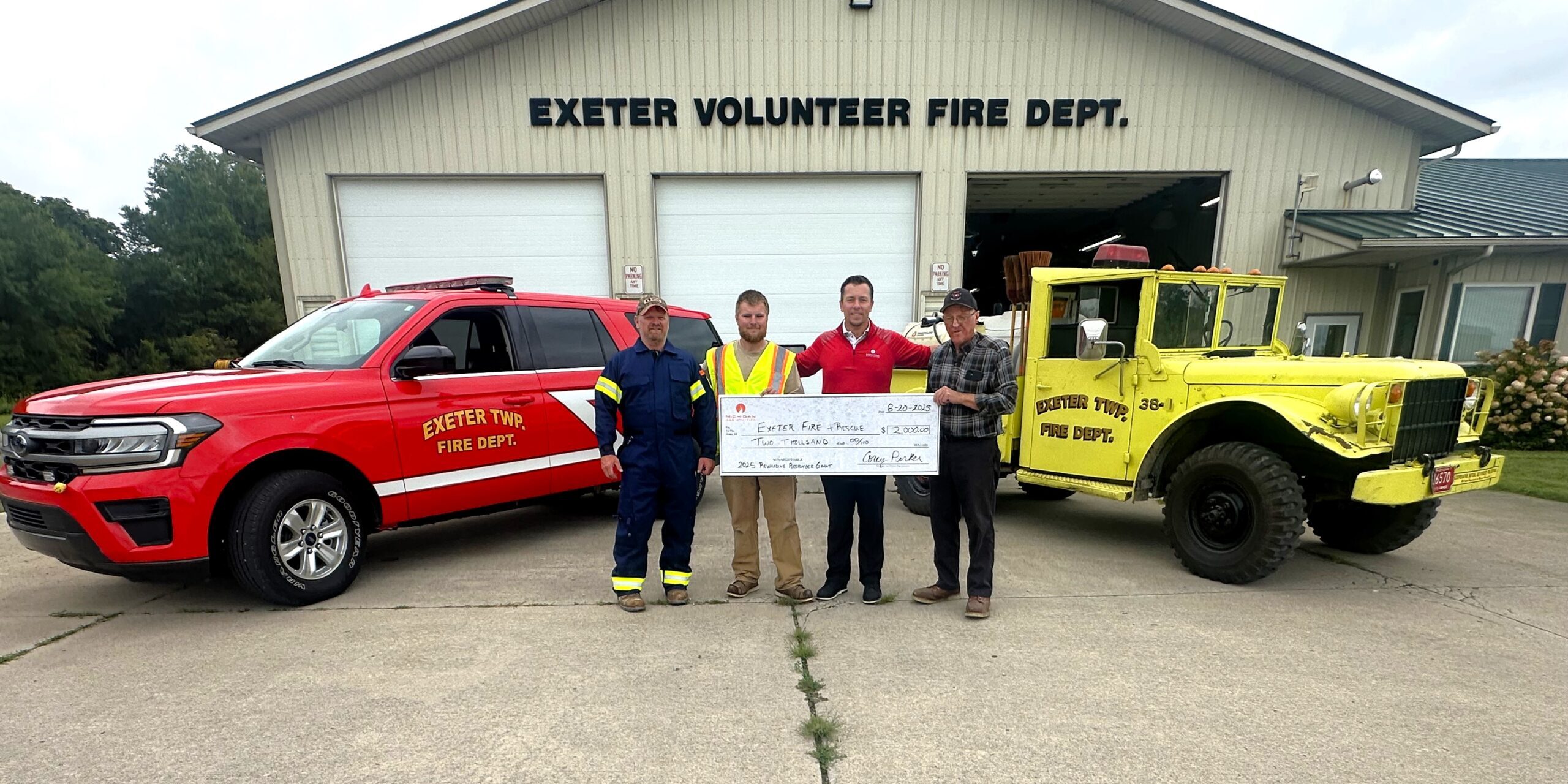 MGU employees hold a large ceremonial check while standing next to firefighters from the Exeter Fire Department.