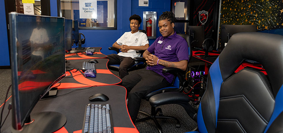Two young adults sit and smile for a photo inside a Boys and Girls Club computer lab.