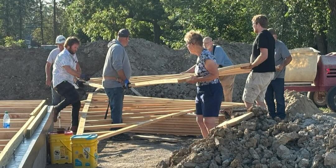 A group of volunteers works to frame a new construction home on a sunny day.