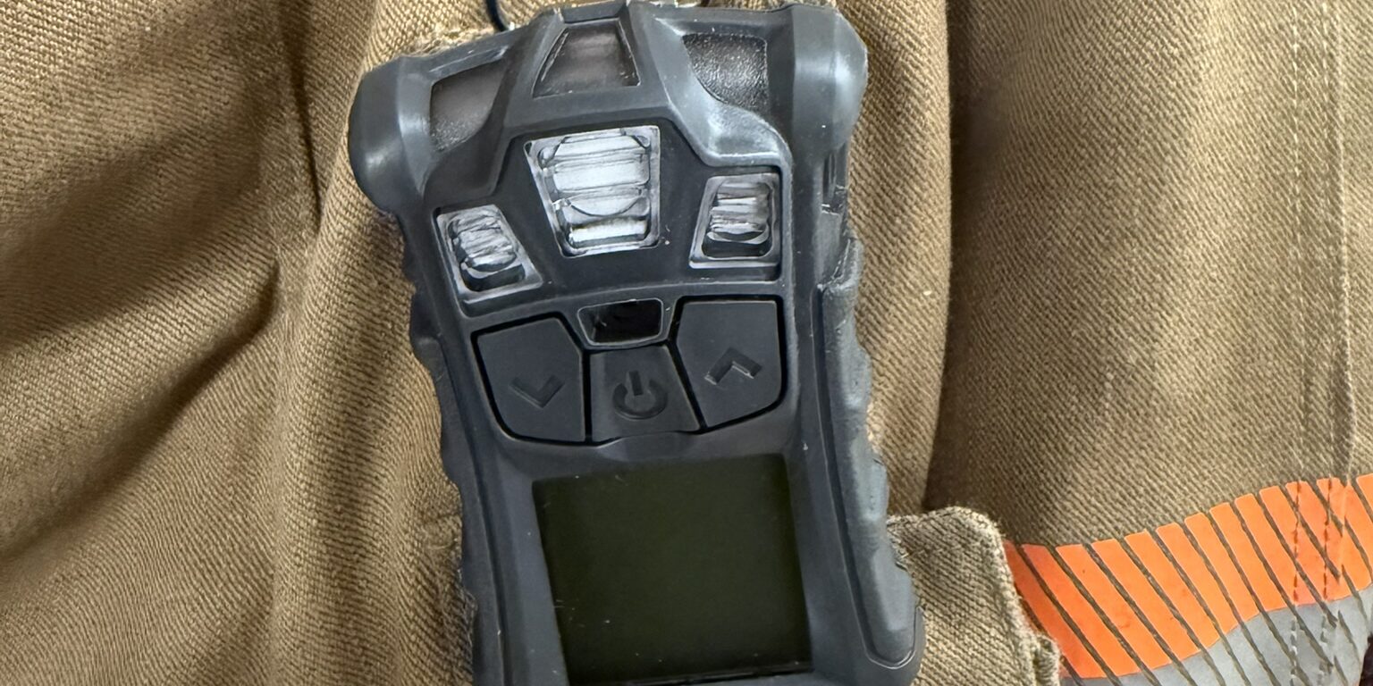 A small black multi-gas detector sits clipped onto a pocket of a firefighter's jacket.